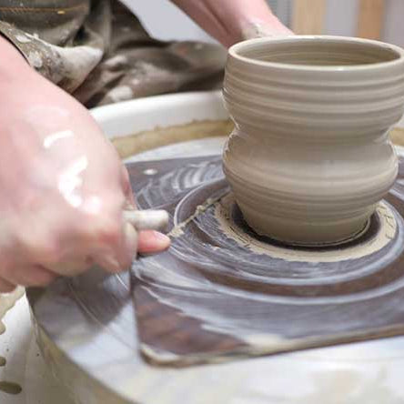 Alli Parrett trimming a curvy cup from the wheel.